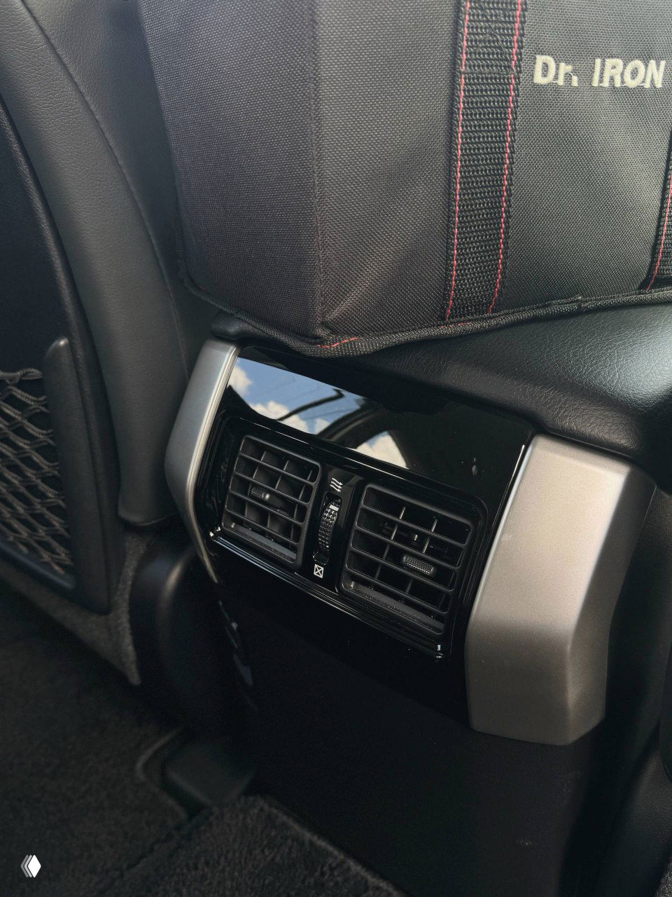 Крупный план задней вентиляционной решетки между передними сиденьями, вид на дефлектор и отделку центральной консоли со стороны пассажиров.