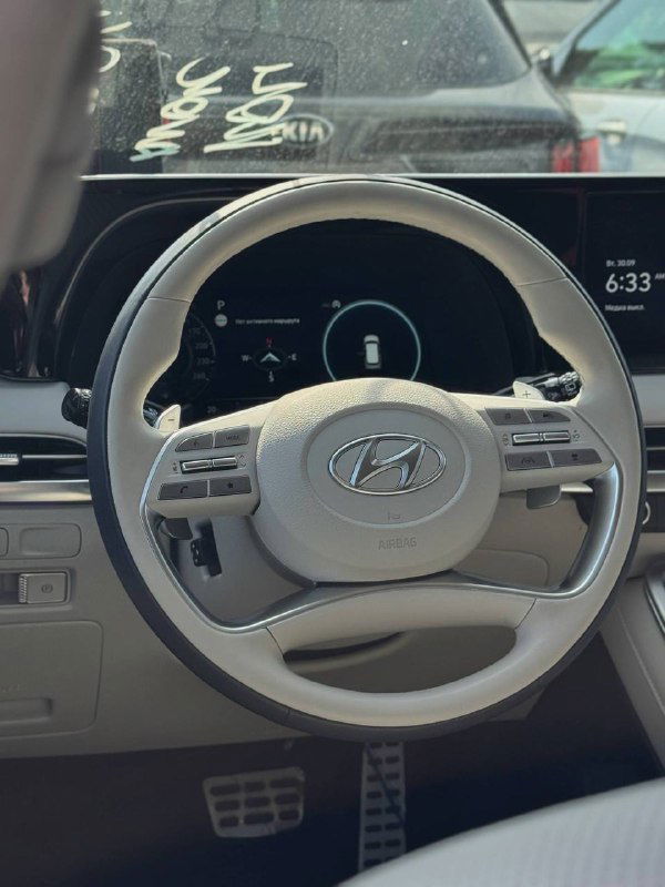 Салон: руль с логотипом Hyundai и цифровая приборная панель, часть торпедо и вид с места водителя на светлую отделку интерьера автомобиля.