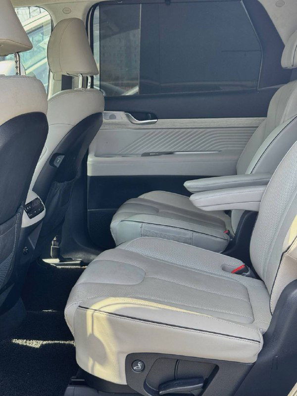 Второй ряд сидений Hyundai Palisade: два капитанских кресла, подлокотник и простор для ног, светлая отделка и вид на дверную панель внутри автомобиля.