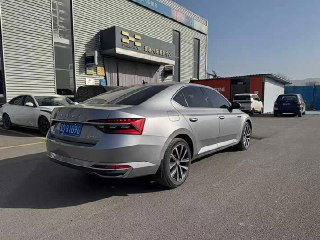 Skoda Superb 2022 — вид сзади и сбоку на парковке дилера в Китае; видно заднюю оптику, бампер и часть здания сервисного центра на фоне.