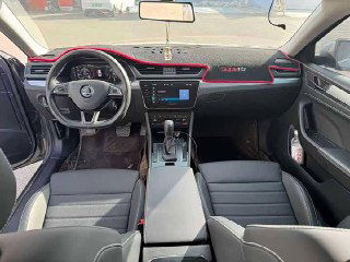 Интерьер Skoda Superb: вид салона спереди — руль, центральная консоль с экраном и селектор КПП; чёрные сиденья и элементы отделки.