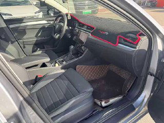 Передняя пассажирская зона Skoda Superb: торпеда с декоративной красной окантовкой, коврики и открытая дверь при осмотре салона на стоянке дилера.