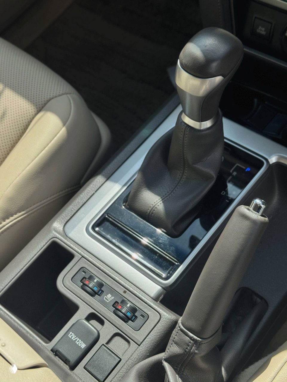 Рычаг переключения передач и ручной тормоз в интерьере Toyota Land Cruiser Prado 2021; видно элементы отделки, подстаканники и регуляторы обогрева сидений