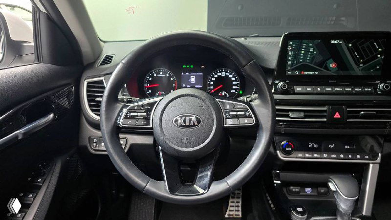 Крупный план рулевого колеса KIA Seltos, панель приборов и центральный экран, видны элементы управления на руле