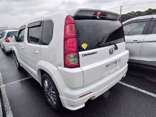 Задний ракурс белого Honda Crossroad 2008 на ярде, видна задняя оптика, багажная дверь и шильдик модели Crossroad.