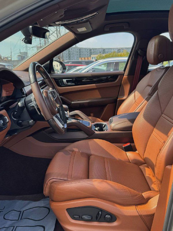 Передняя часть салона Porsche Cayenne: оба передних сиденья, центральный подлокотник и часть приборной панели, интерьер в коричневой коже.