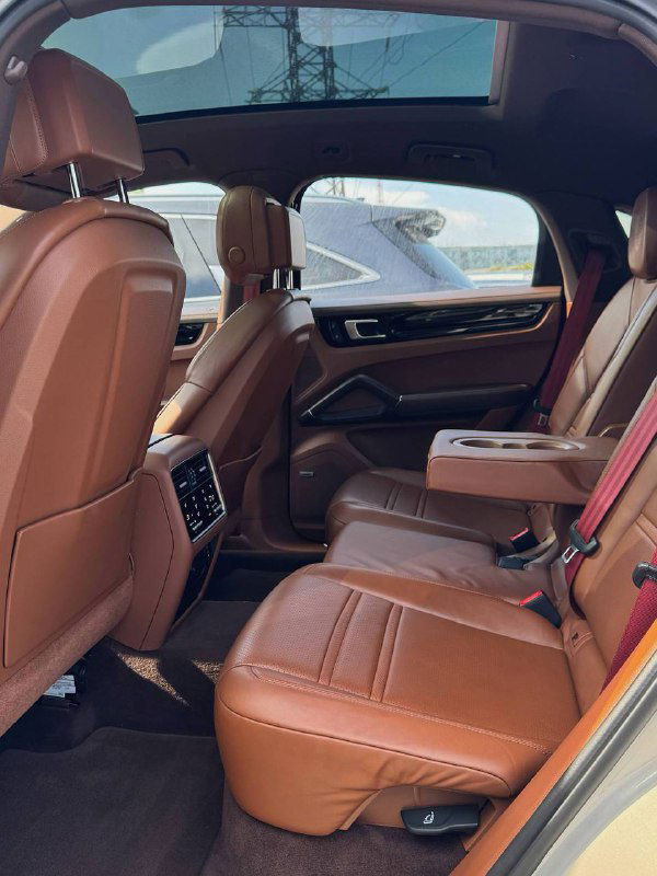 Задний ряд салона Porsche Cayenne: коричневые кожаные сиденья, пространство для пассажиров и опущенный центральный подлокотник с подстаканниками.