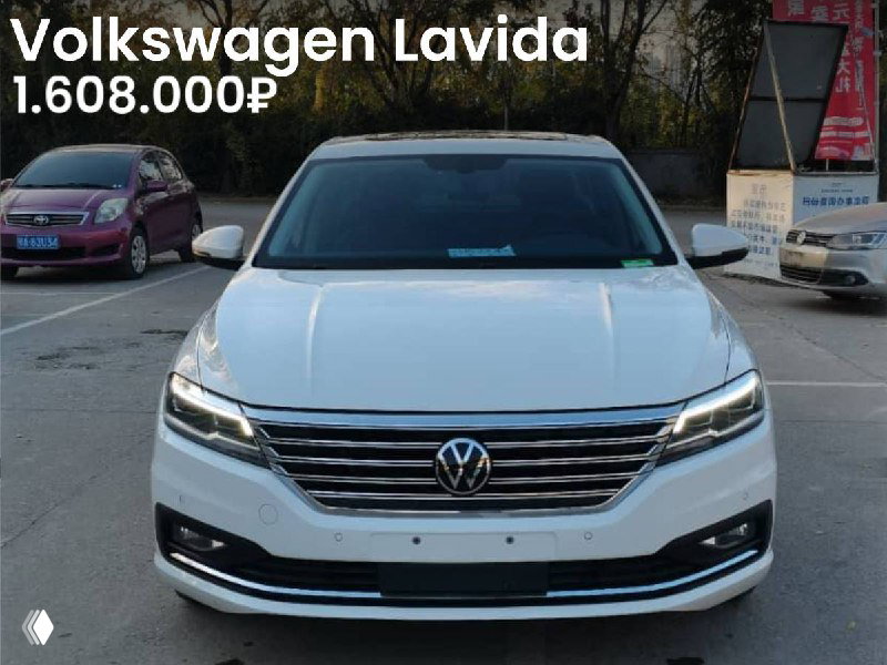 Фронтальный вид белого Volkswagen Lavida 2021 года на открытой стоянке: видна решётка радиатора, фары и часть окружающей парковки, цена 1.608.000₽ видна в объявлении.