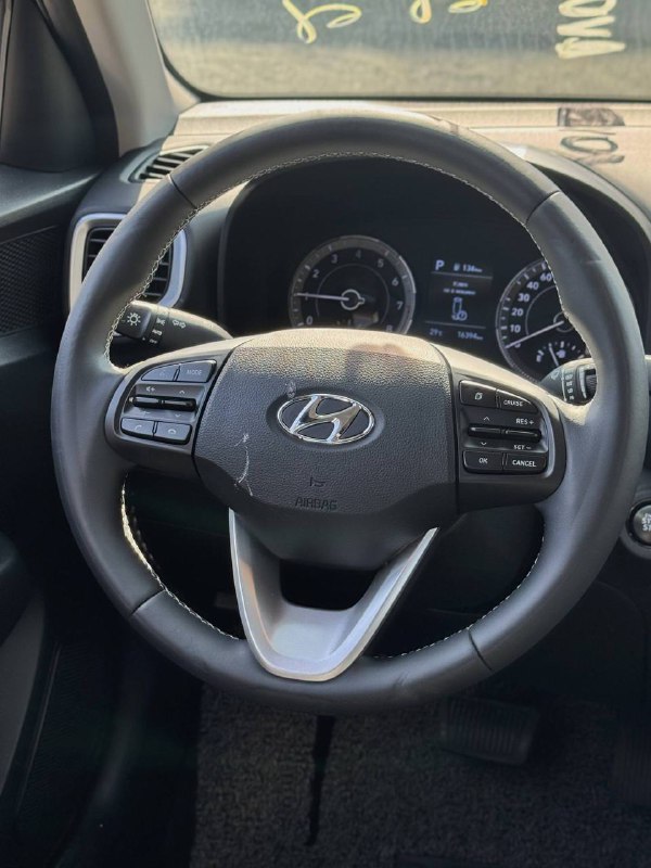 Крупный план рулевого колеса Hyundai Venue с логотипом, вид на комбинацию приборов и мультируль в интерьере автомобиля.