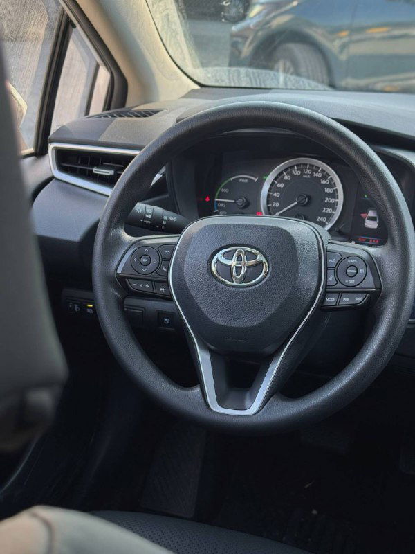 Рулевое колесо и приборная панель Toyota Corolla 2022: логотип Toyota на руле, спидометр и тахометр видны крупным планом.