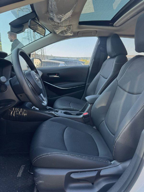 Передние сиденья и интерьер Toyota Corolla 2022: чёрная обивка, центральный подлокотник и панорамная крыша, крупный план салона.