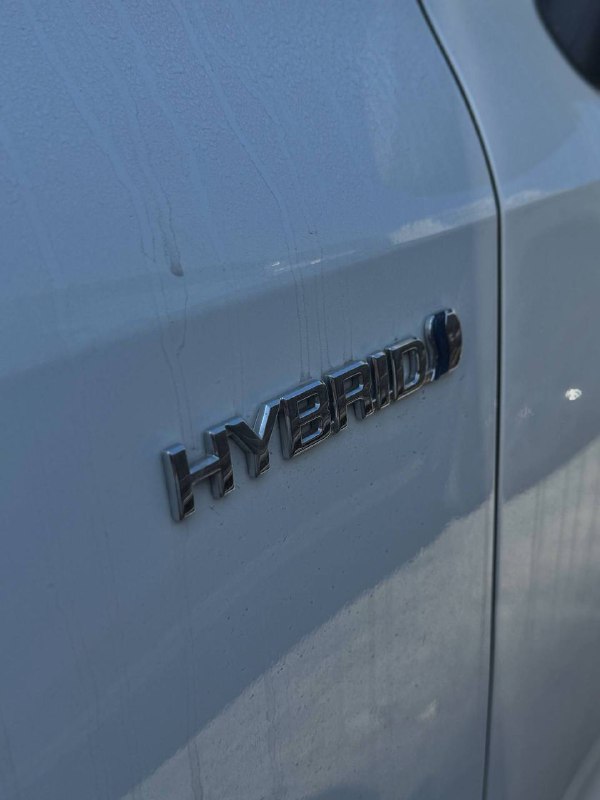 Крупный план эмблемы HYBRID на крыле белой Toyota Corolla 2022, подчёркивающий гибридную силовую установку автомобиля.