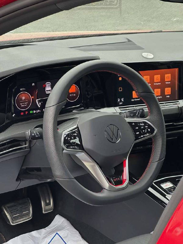 Руль и передняя панель Volkswagen Golf GTI с фирменным шильдиком, вид салона со стороны водителя, многофункциональные кнопки на руле.