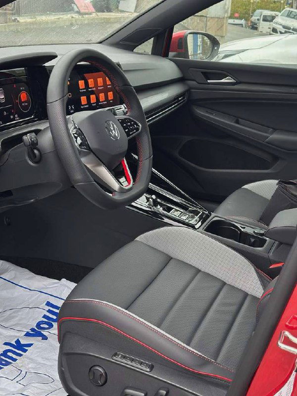 Интерьер передней части салона Volkswagen Golf GTI: водительское сиденье, панель приборов, декоративные элементы и отделка с контрастной прострочкой.