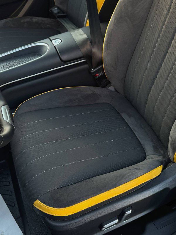 Переднее сиденье Ora 03 GT: текстильная обивка с жёлтыми вставками по кромке, вид на регулировки сиденья и часть центрального тоннеля, чистое состояние салона.