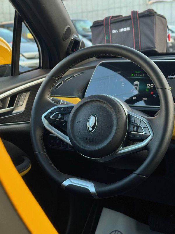 Крупный план руля и центральной части приборной панели в Ora 03 GT: элементы управления на руле, цифровая приборная панель и декоративные вставки жёлтого цвета.