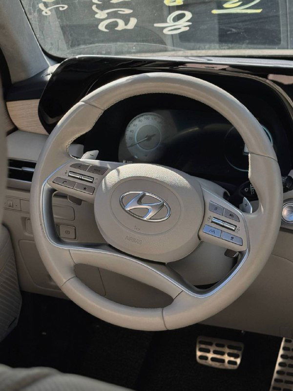 Салон автомобиля: крупный план многофункционального руля Hyundai Palisade светлого тона, видны элементы управления и подушки безопасности на руле.