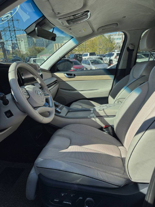 Вид на передний пассажирский отсек и водительское место Hyundai Palisade с кожаными светлыми сиденьями и общей компоновкой салона в натуральном освещении.