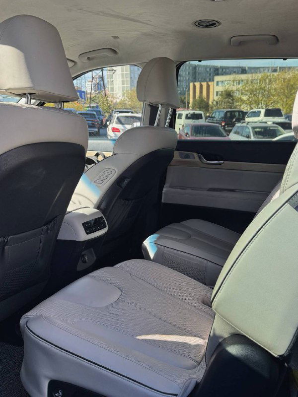 Вид заднего ряда сидений Hyundai Palisade, показаны просторный тоннель и подголовники, салон на фоне припаркованных автомобилей.