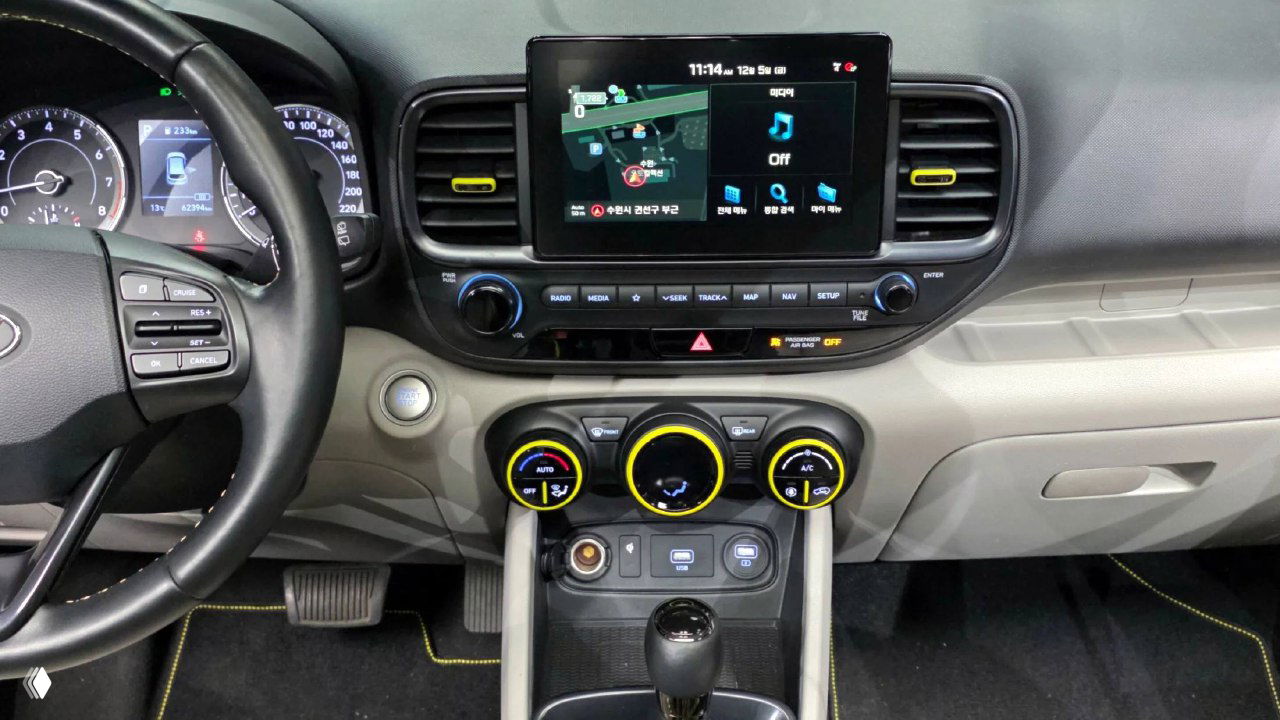 Центральная консоль Hyundai Venue: экран мультимедиа, круглые регуляторы климата с жёлтой окантовкой и элементы управления под экраном, общий план.