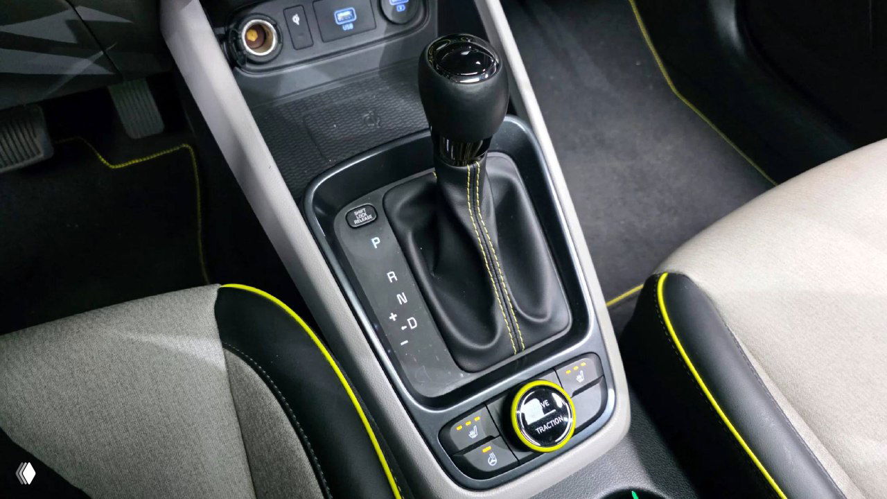 Крупный план селектора коробки передач Hyundai Venue: ручка переключения, ручной тормоз и декоративная прострочка на обивке сидений вокруг консоли.