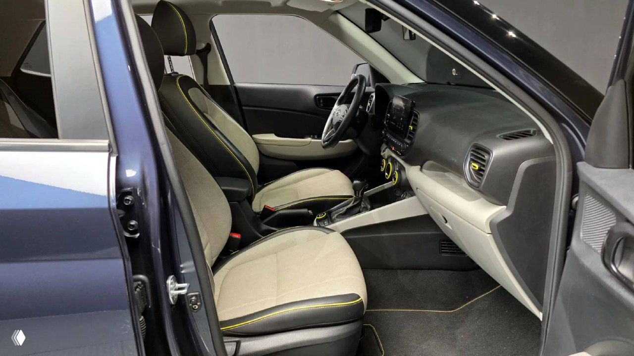 Вид на передние сиденья и дверной проём Hyundai Venue: открытая передняя дверь, панели обивки с контрастной прострочкой и пространство водителя в профиль.