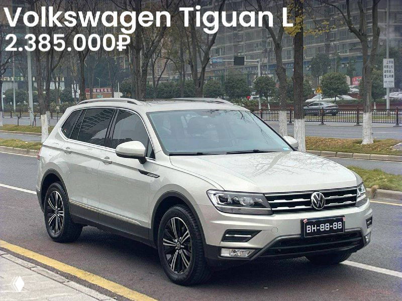 Белый Volkswagen Tiguan L, боковой/угловой вид на городской дороге, указанная на фото цена 2.385.000₽, автомобиль на парковке.