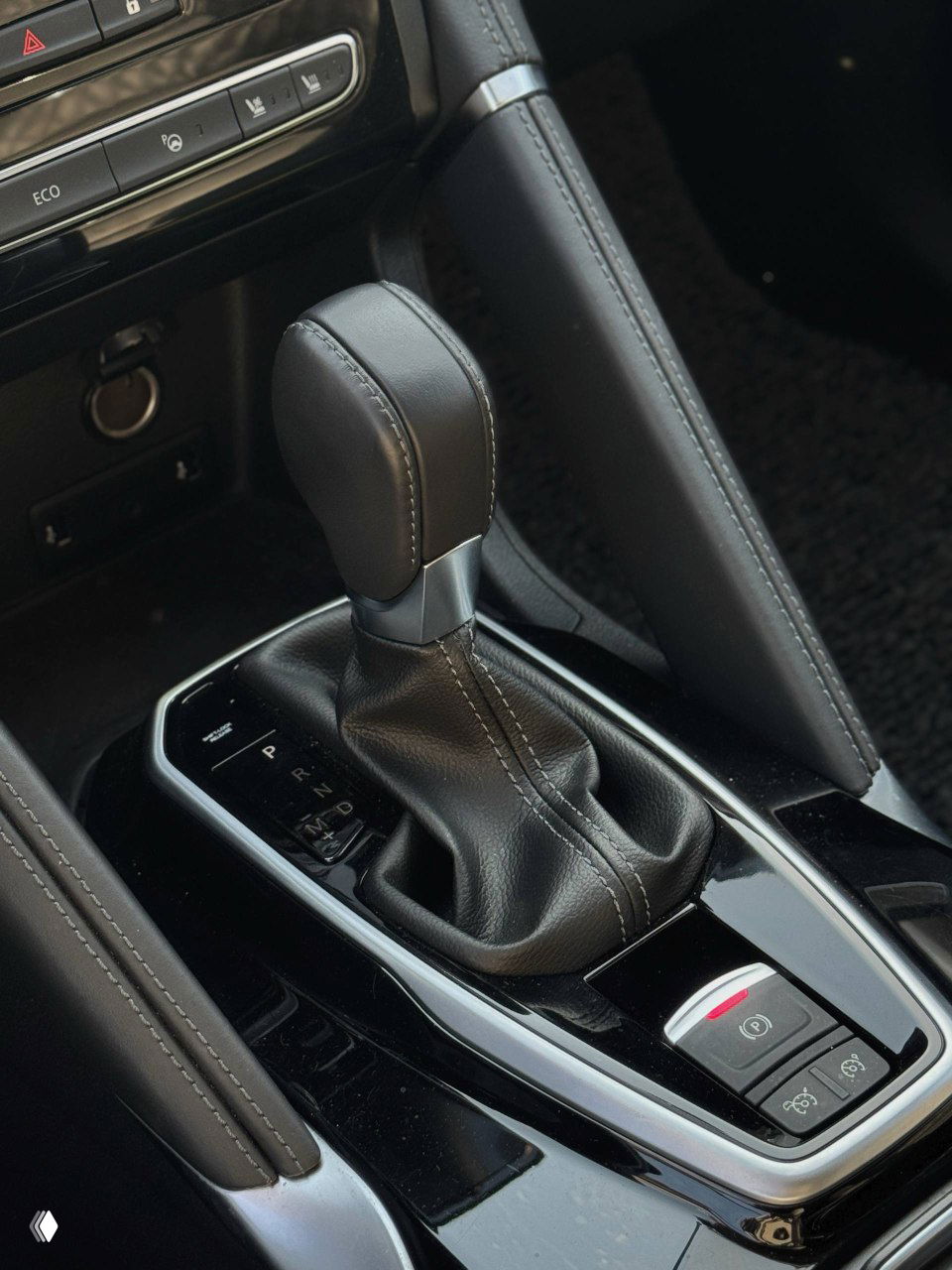 Крупный план рукояти селектора вариатора и кнопок стояночного тормоза в салоне Samsung QM6, кожаная отделка и декоративные швы