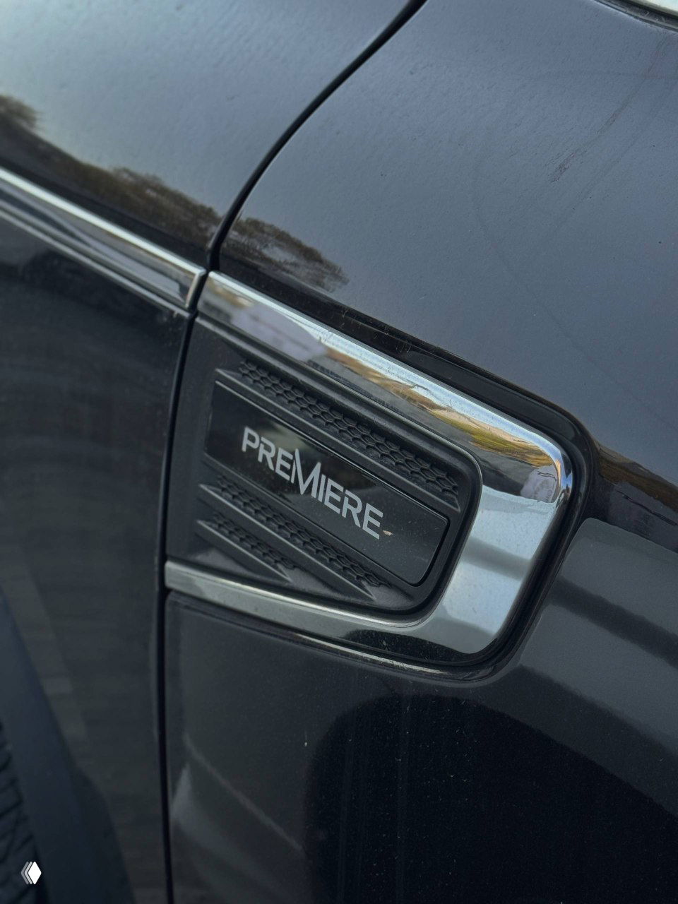 Крупный план шильдика "PREMIERE" на левом крыле чёрного Samsung QM6, хромированная окантовка и фрагмент лаковой поверхности автомобиля