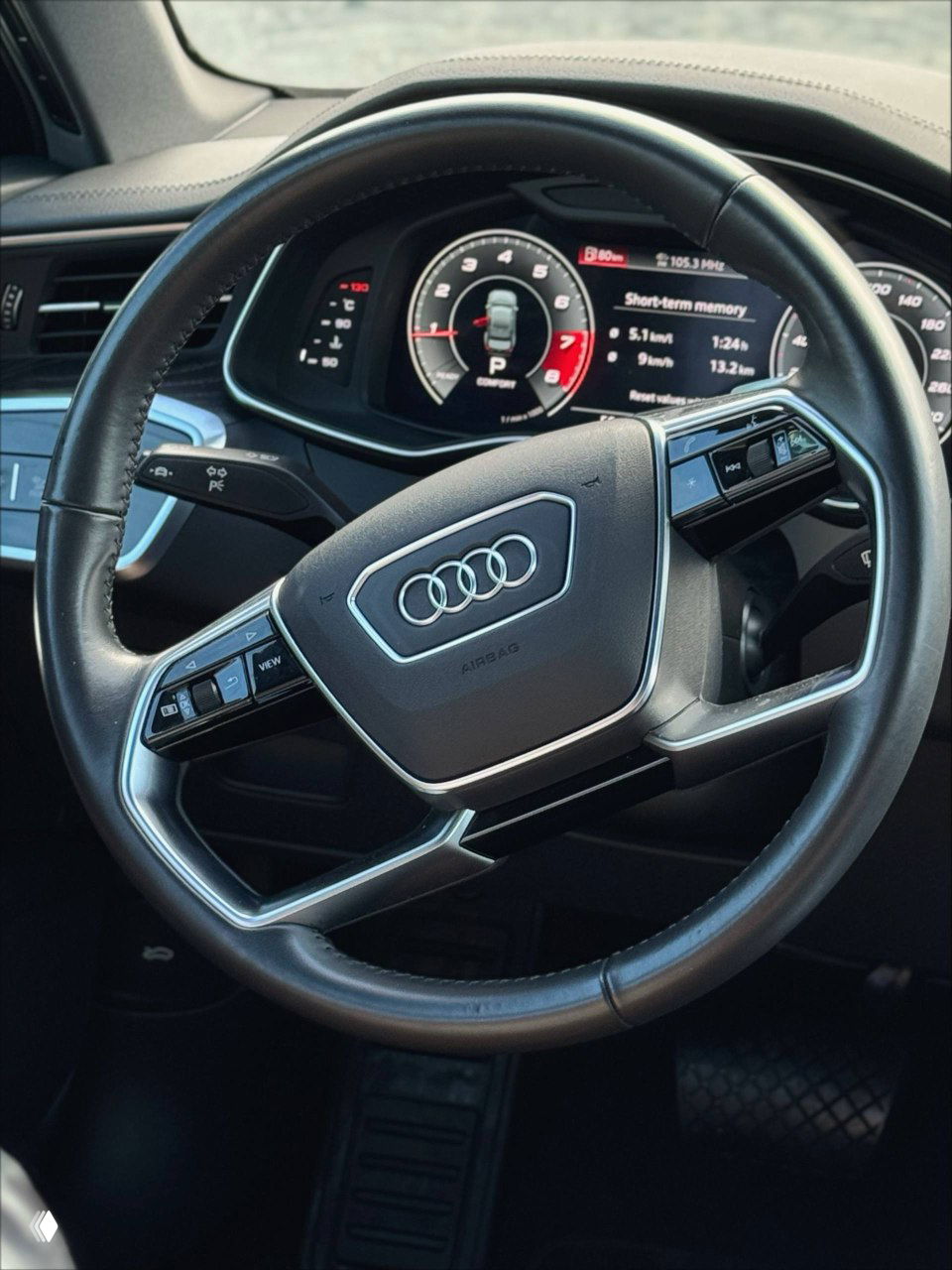 Крупный план рулевого колеса Audi с эмблемой четырех колец, мультируль с кнопками управления и цифровая панель приборов на фоне — фото салона для объявления.