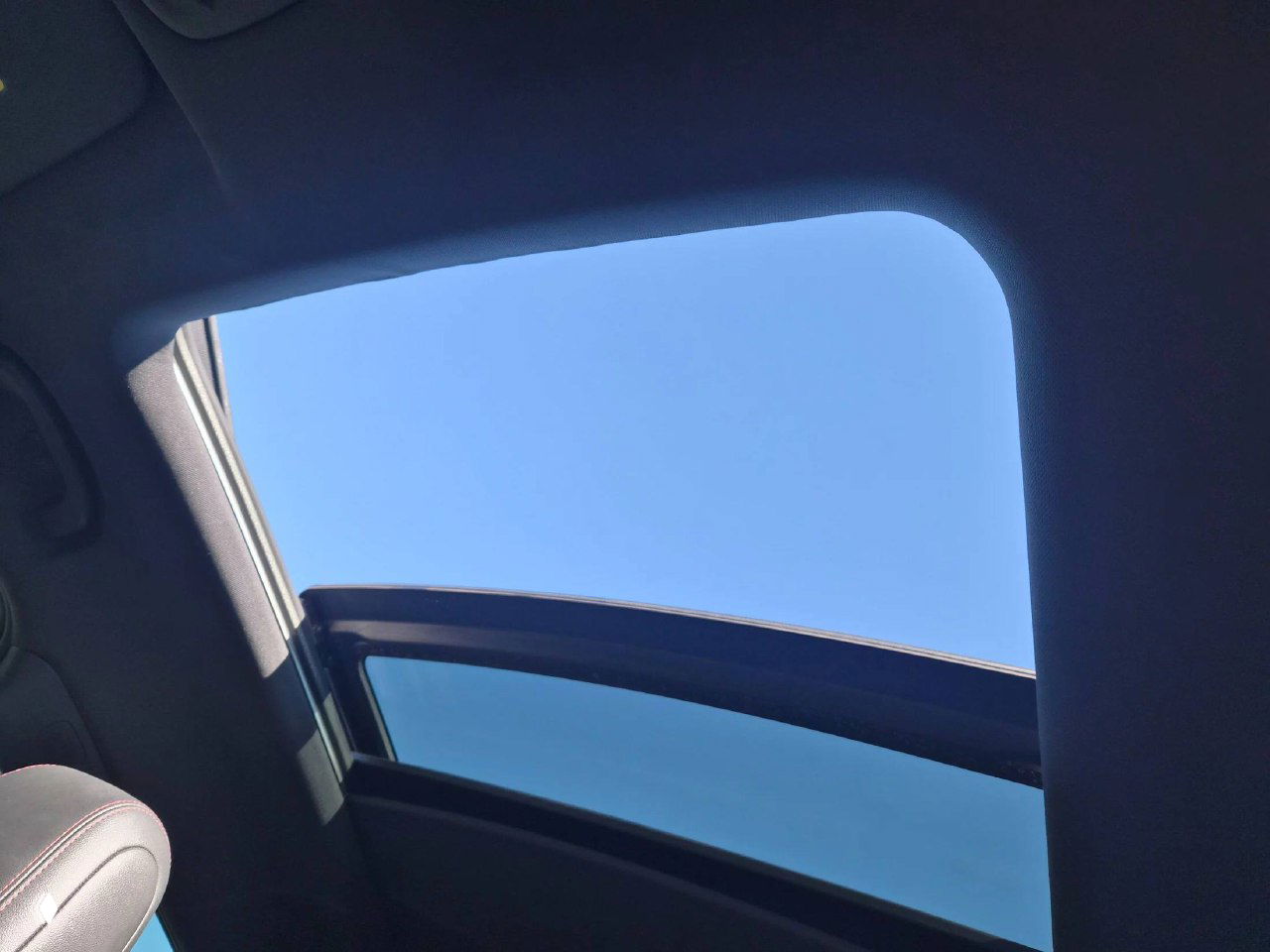 Открытый люк в крыше салона Chevrolet Trailblazer, вид на небо и часть дверного проёма, демонстрация опции панорамного освещения и состояния уплотнений.