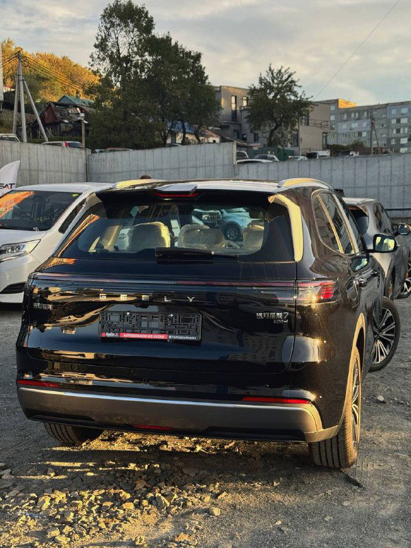 Задняя часть чёрного Geely Galaxy Starship 7 2025, вид сзади на парковке, заметна оптика, шильдик и форма багажника в городском окружении