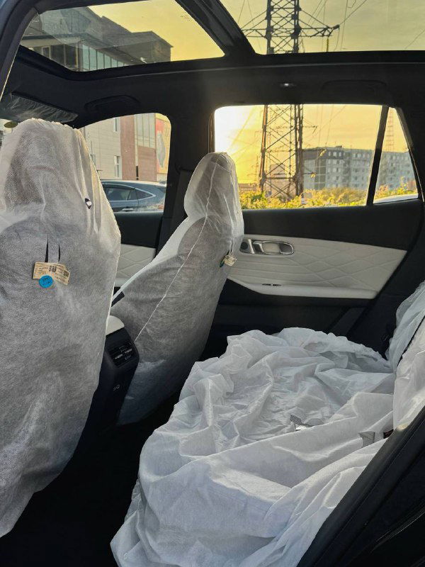 Задние сиденья Geely Galaxy Starship 7 в защитных упаковках, панорамная крыша сверху и элементы интерьера на фоне городского пейзажа