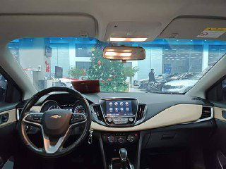 Интерьер Chevrolet Monza: вид на руль, приборную панель и мультимедиа-экран; салон бежево-чёрной отделки, приборы подсвечены.