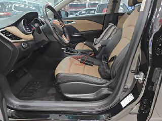 Передние сиденья Chevrolet Monza в бежево-чёрной комбинации, открытая дверь водителя, видна центральная консоль и рычаг АКПП на фоне автосалона.