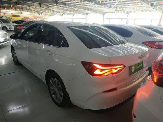 Задняя часть белого Chevrolet Monza 2022 в автосалоне, включены LED-фонари, вид кузова и багажника с правого кормового угла автомобиля.