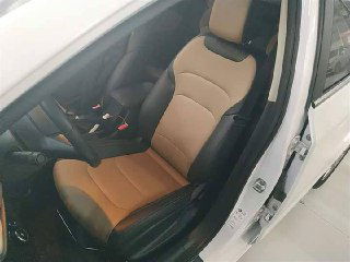 Переднее водительское сиденье Chevrolet Monza 2022 с комбинированной бежево-чёрной обивкой в открытой дверь салона, вид сбоку на посадку водителя.