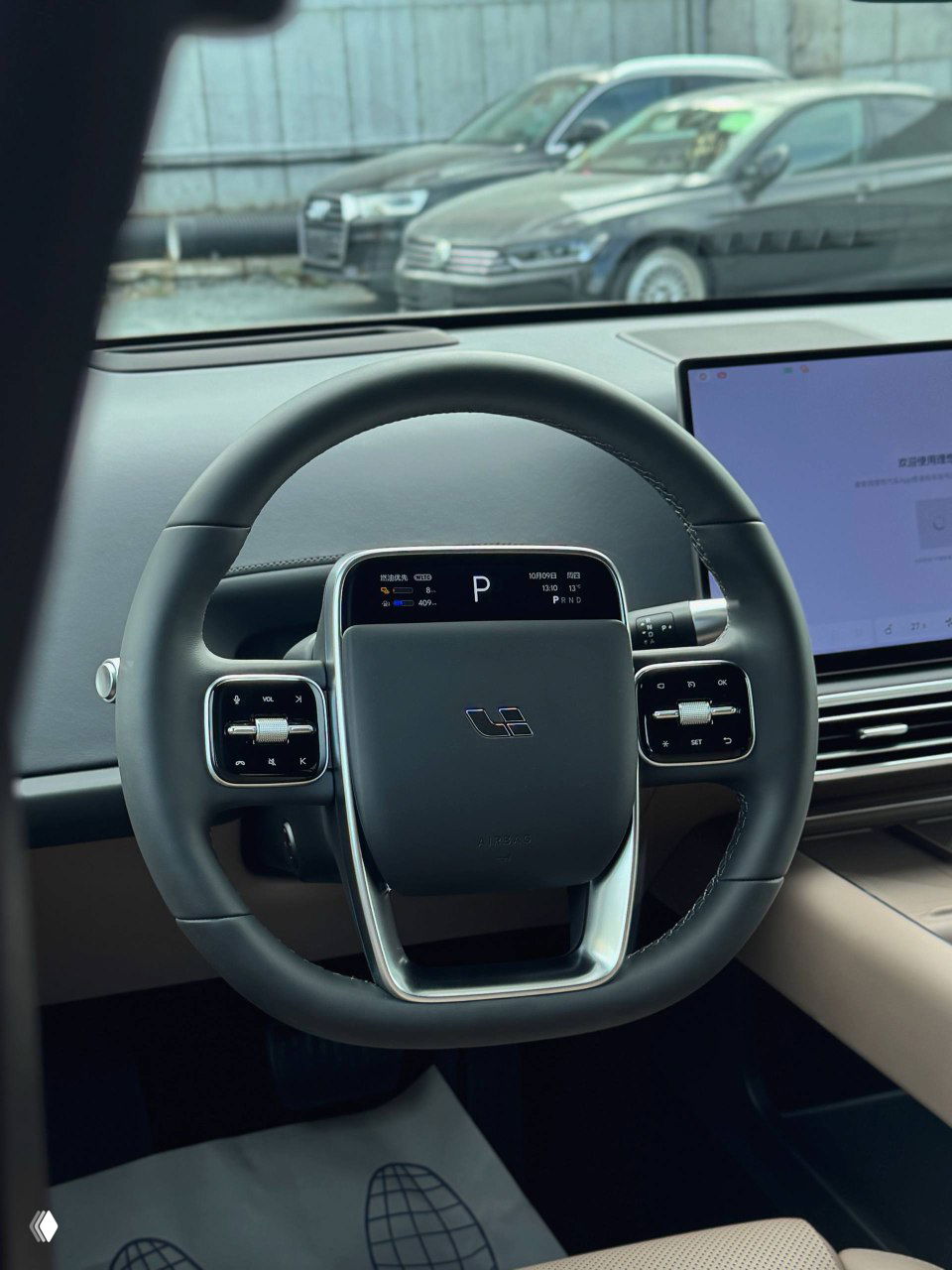 Интерьер: руль и приборная панель Lixiang L6, современный компактный руль с логотипом, цифровая панель и большой экран мультимедиа, вид в салон с водительской стороны.