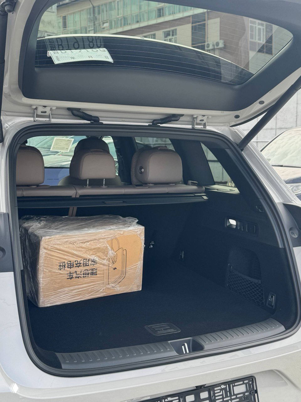 Вид через задние окна на интерьер Lixiang L6 и часть багажного отсека, кадр подчёркивает отделку сидений и панорамный люк, автомобиль на открытой стоянке.