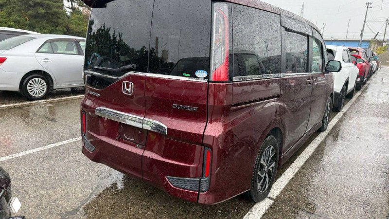 Задний ракурс Honda Stepwgn 2019 бордового цвета на парковке: видны багажная дверь, фонари, эмблема Honda и парковочные маркировки.