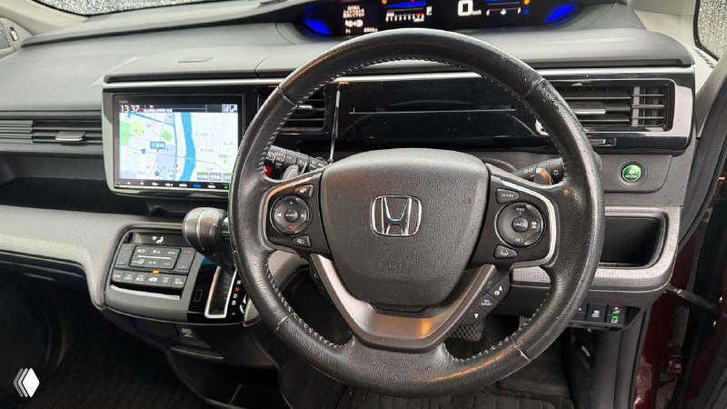 Руль и приборная панель Honda Stepwgn 2019: крупный план руля с логотипом Honda, дисплей, элементы управления и часть торпедо.