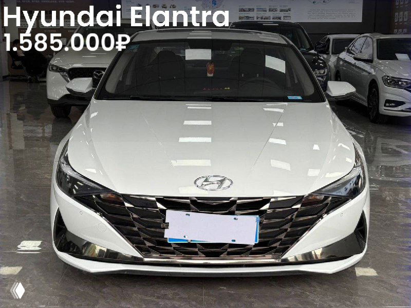 Белый Hyundai Elantra в выставочном зале, вид спереди сверху; на фото видно салон за лобовым стеклом и цену 1.585.000₽.