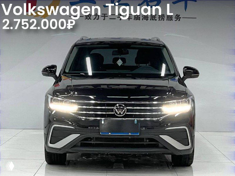Volkswagen Tiguan L чёрного цвета в салоне, фронтальный вид с включёнными ходовыми огнями, на картинке указана цена 2.752.000₽.