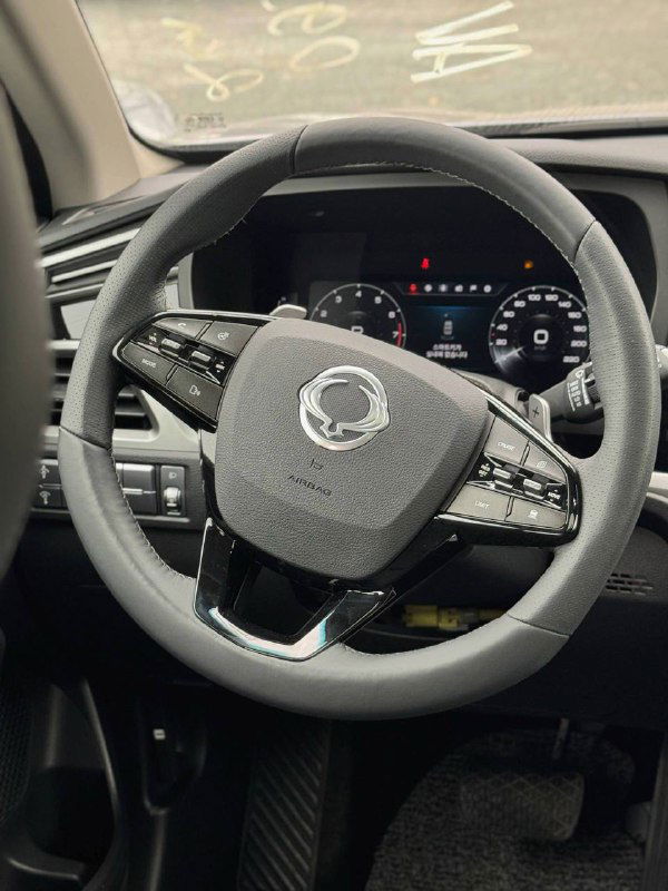 Крупный план руля и приборной панели SsangYong Korando с логотипом на руле, видны кнопки мультимедиа и циферблаты спидометра.