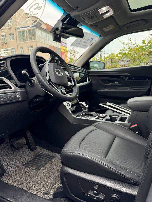 Общий вид передней части салона SsangYong Korando: водительское кресло, пассажирское место, руль и общая отделка интерьера.