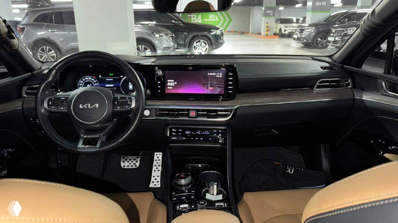 Салон KIA K5 2023: панорамный вид на рулевую колонку, мультимедийный дисплей и торпедо, коричневая кожа сидений частично видна