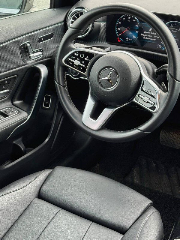 Салон Mercedes A200d, вид на руль и панель водителя; показана обшивка дверей, органы управления и частично приборная панель автомобиля.