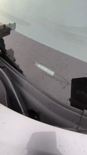 Крупный план ветрового стекла Nissan Kicks, видна заводская бирка или серийный номер на стекле, капли воды и отражения.