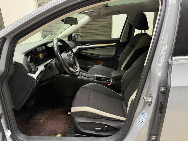 Салон Volkswagen Golf 2021: передняя часть салона, рулевое колесо, приборная панель и посадочные места водителя и пассажира, чёрная и серая обивка.