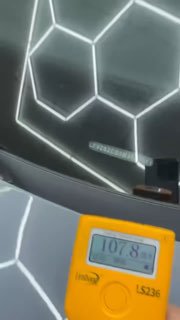 Жёлтый измерительный прибор на фоне потолочных светильников и части лобового стекла автомобиля, на экране отображено значение 107.8 — фото в шоуруме.